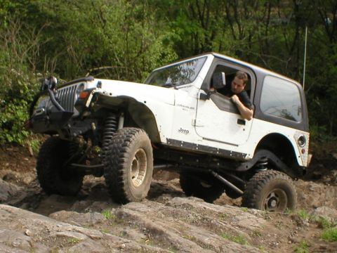 1978 Ford Bronco - A white Jeep Wrangler navigates a rocky trail with a driver behind the wheel.
