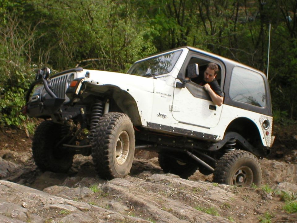 White Jeep Wrangler climbing rocks, driver visible