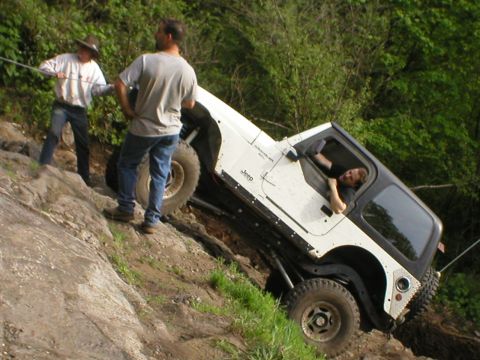 1978 Ford Bronco - Jeep Wrangler struggling on a steep, rocky off-road trail with assistance from two individuals.
