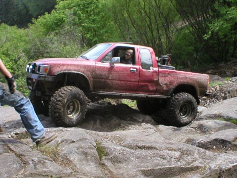 1978 Ford Bronco - A red pickup truck with oversized tires is shown off-roading over large rocks.