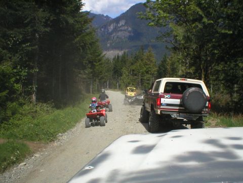1978 Ford Bronco - A 1978 Ford Bronco leads a group of ATVs down a wooded dirt road with mountains in the background.