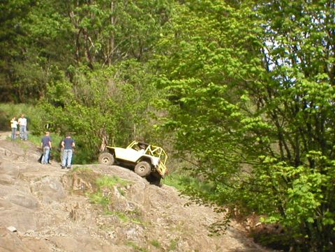 1978 Ford Bronco - An off-road vehicle navigates a steep, rocky incline surrounded by lush green trees.