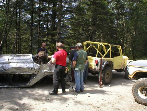 1978 Ford Bronco - Several individuals are working on a damaged vehicle chassis next to a yellow Jeep and another truck.