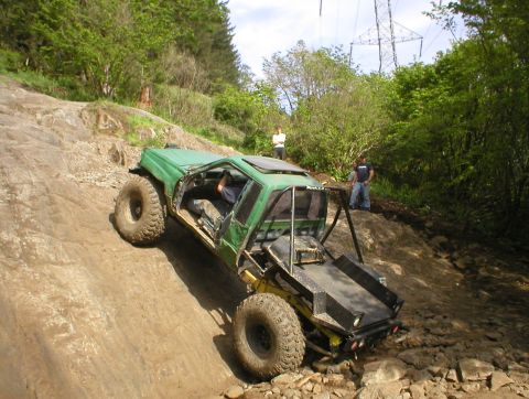 1978 Ford Bronco - A modified green off-road vehicle navigates a steep, rocky trail with two people observing.