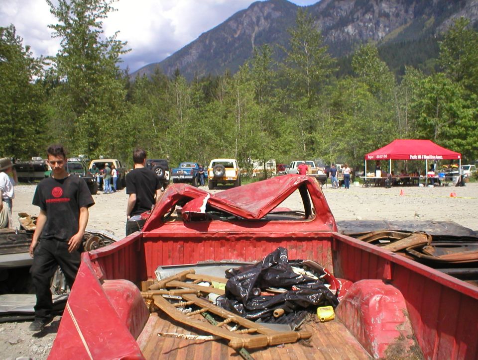 Red pickup truck bed filled with debris, with other vehicles and people in background