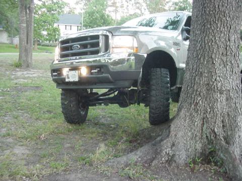 2000 Chevrolet Tahoe - A lifted pickup truck is parked on a grassy area next to a large tree.