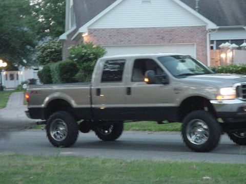 2000 Chevrolet Tahoe - A lifted pickup truck drives down a suburban street, kicking up some dust.