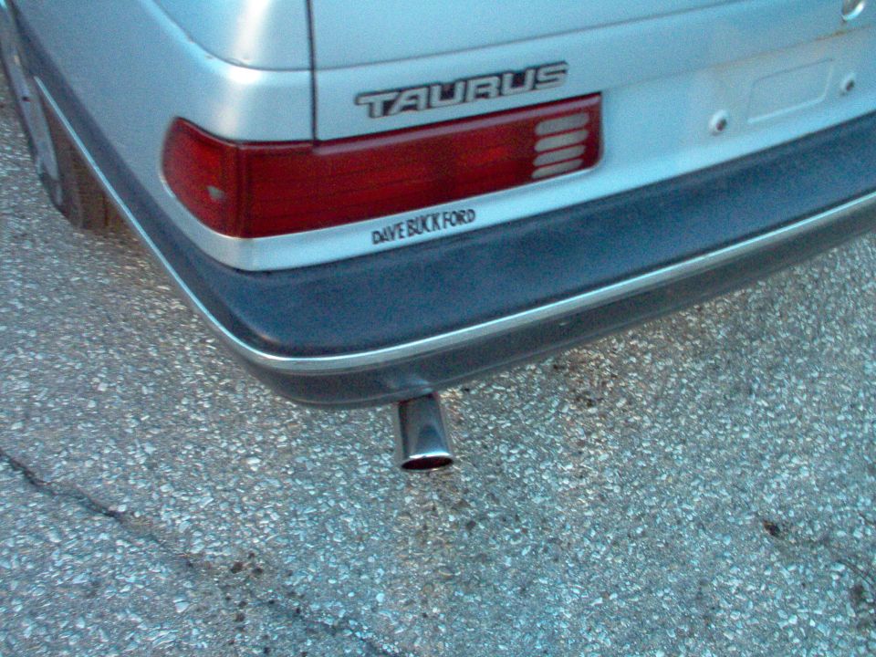 Silver 1990 Ford Taurus rear with 'TAURUS' badge and 'DAVE BUCK FORD' sticker