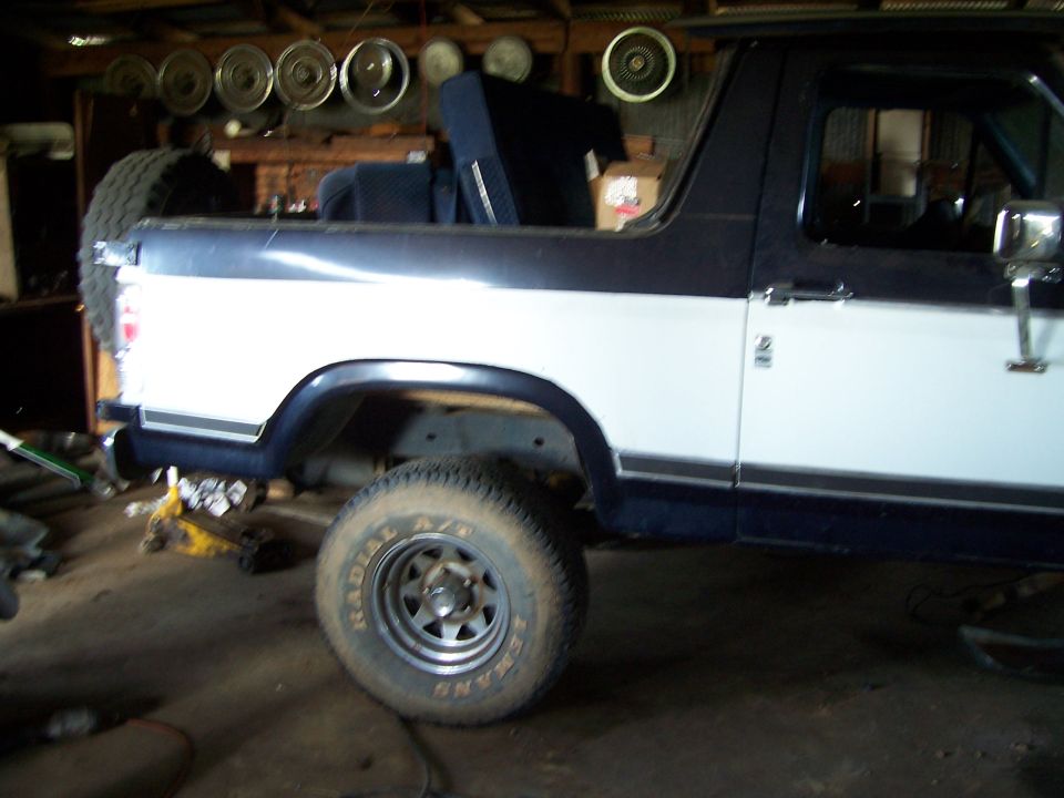 Blue and white lifted Ford Bronco with top off parked inside a workshop