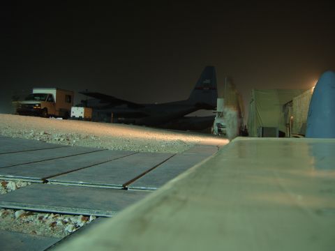 1988 Ford Bronco - A white utility truck is parked near a large military cargo plane on a tarmac at night.