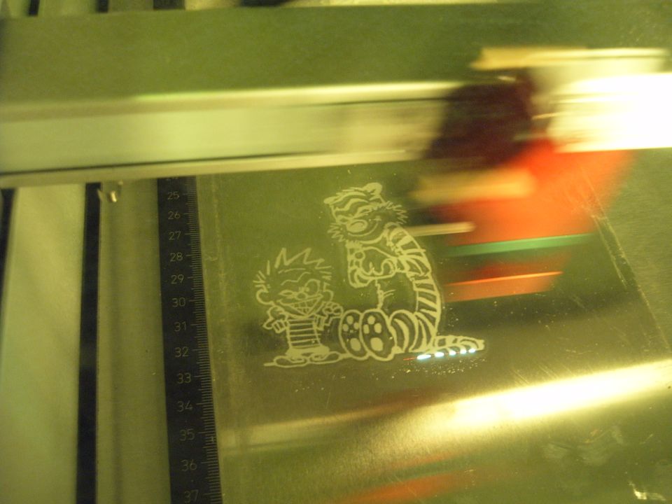 Calvin and Hobbes sticker etched onto a metallic surface next to a ruler. SUPERMOTORS.NET logo visible