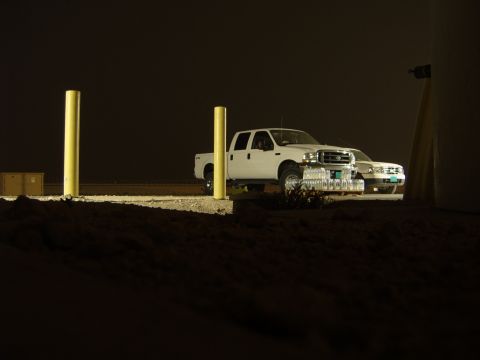 1988 Ford Bronco - Two trucks are parked outside at night, illuminated by artificial lights.