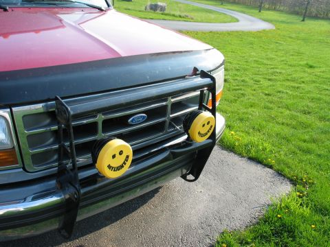 1995 Ford Bronco - The front grille of a red Ford truck is visible, yellow fog lights with smiley faces.