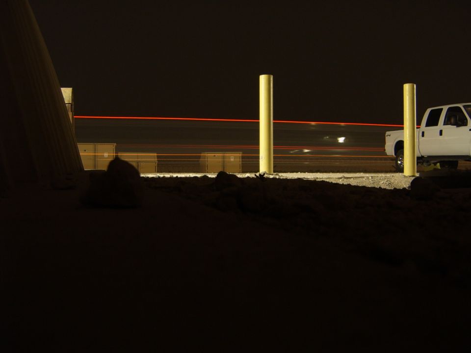 white pickup truck parked at night, red light streaks in background