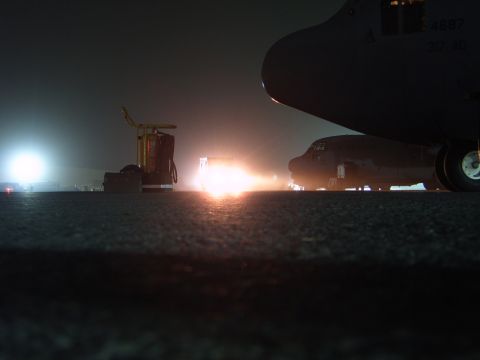 1988 Ford Bronco - An aircraft is seen on a tarmac at night, illuminated by bright lights, with a fire extinguisher cart nearby.