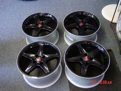 1985 Ford Mustang - A set of four aftermarket wheels with black faces and silver barrels are displayed on a carpeted surface.