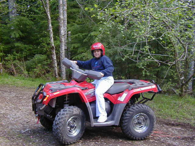 Person in red helmet sitting on a red and gray ATV on a gravel path in the woods