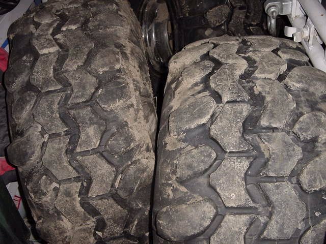 Two muddy off-road tires with aggressive tread patterns are shown up close