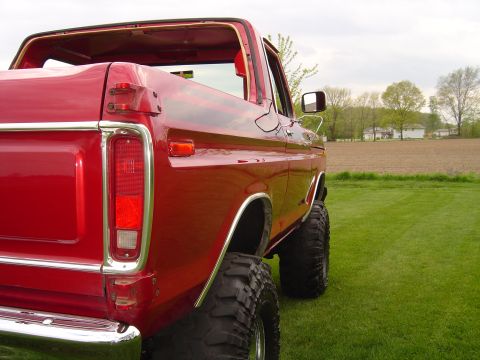 1978 Ford Bronco - Rear view of a red pickup truck with large off-road tires, parked in a grassy field.