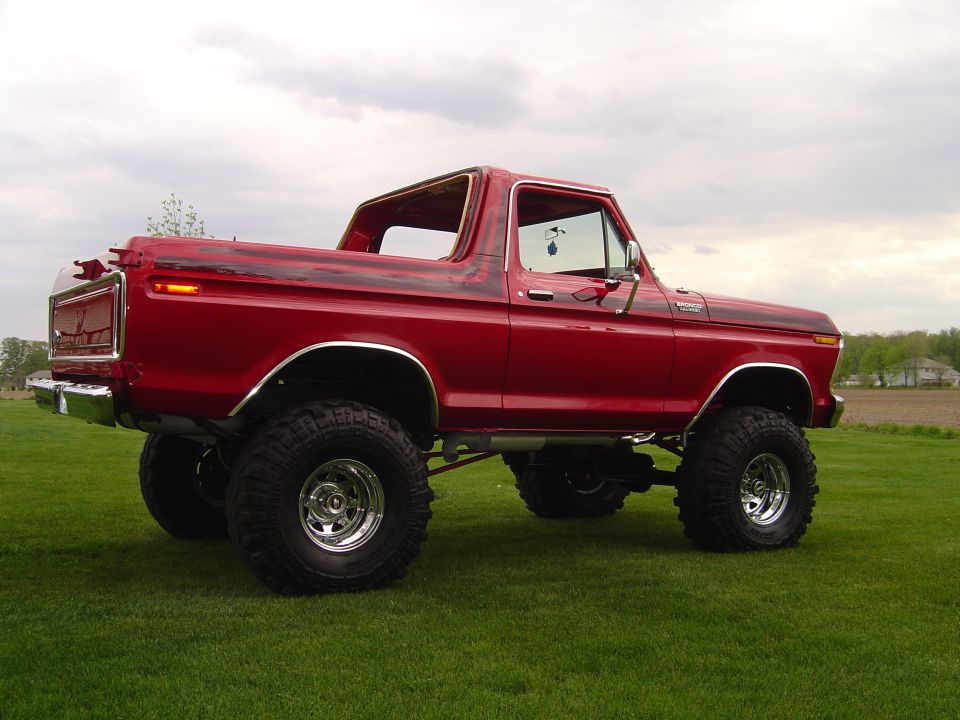 Red 1978 Ford Bronco with lifted suspension and large tires parked on grass