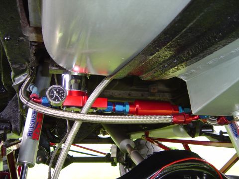 1978 Ford Bronco - Underbody close-up of a fuel system mounted on the frame beside a bare aluminum fuel tank: a red-anodized fuel pump and inline filter, a re…