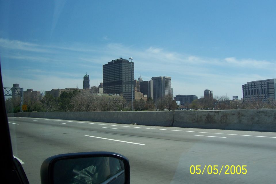 Highway view of city skyline with a concrete barrier and a side mirror reflecting interior
