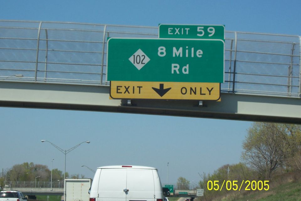 Highway exit sign for 8 Mile Rd, Exit 59, with a white van visible below