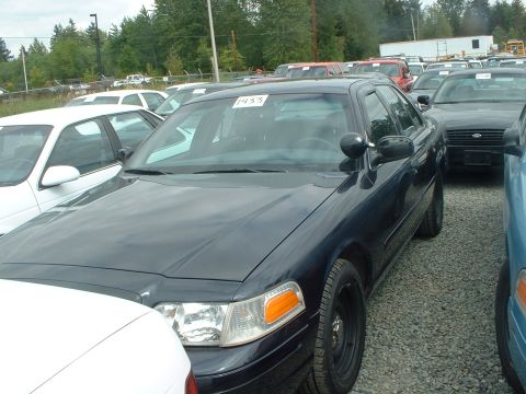 1999 Ford Crown Victoria - A dark blue 1999 Ford Crown Victoria sedan is parked in a lot with other vehicles.