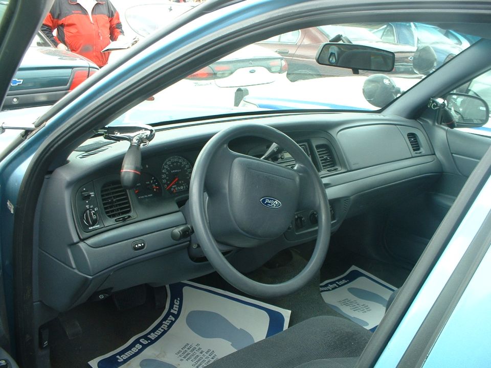 1999 Ford Crown Victoria interior showing dashboard, steering wheel with Ford logo, and floor mats