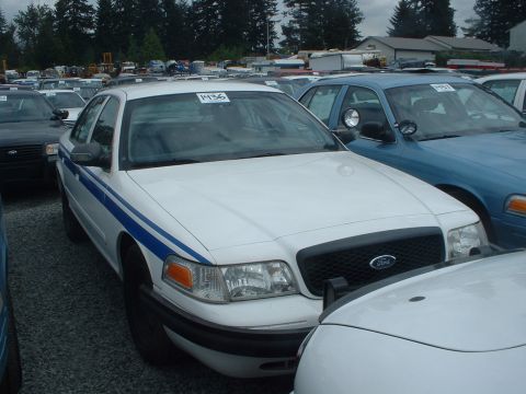 1999 Ford Crown Victoria - A white Ford Crown Victoria with blue stripes is parked in a lot with other vehicles.