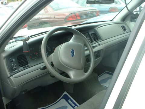 1999 Ford Crown Victoria - Interior view of a 1999 Ford Crown Victoria, showing the dashboard and steering wheel. Other vehicles are visible through the windows.