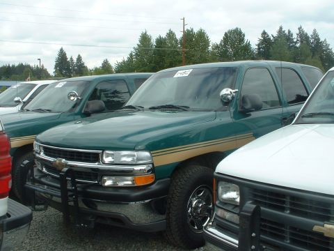 1999 Ford Crown Victoria - Multiple green Chevrolet Tahoes with tan stripes and push bars are lined up, possibly at an auction.