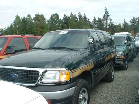 1999 Ford Crown Victoria - A line of SUVs, including a dark green Ford Expedition, are parked outdoors under a cloudy sky.