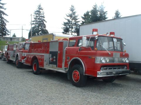 1999 Ford Crown Victoria - Multiple red fire trucks are lined up in a gravel lot.
