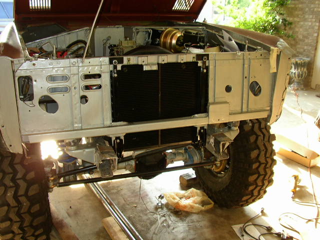 Front of a Ford Bronco with hood open, showing engine bay and radiator. Tires are large and knobby