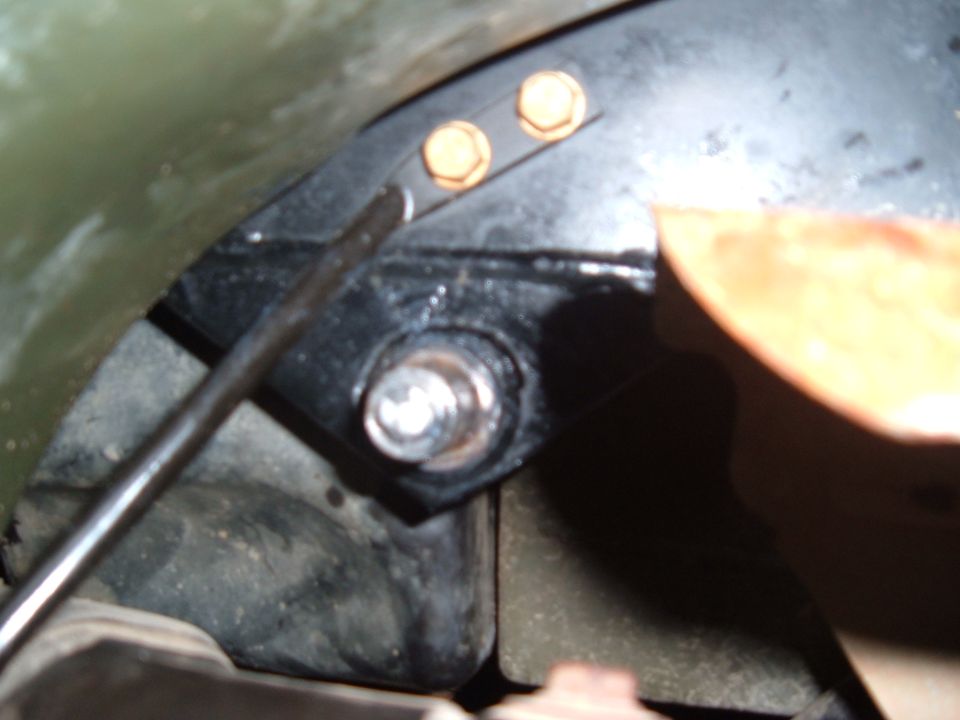 Close-up of a metal bracket with two gold bolts and a silver bolt, attached to a black component. A metal rod is visible