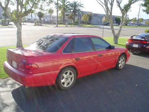 1993 Ford Taurus - A red sedan is parked next to another car in a lot.