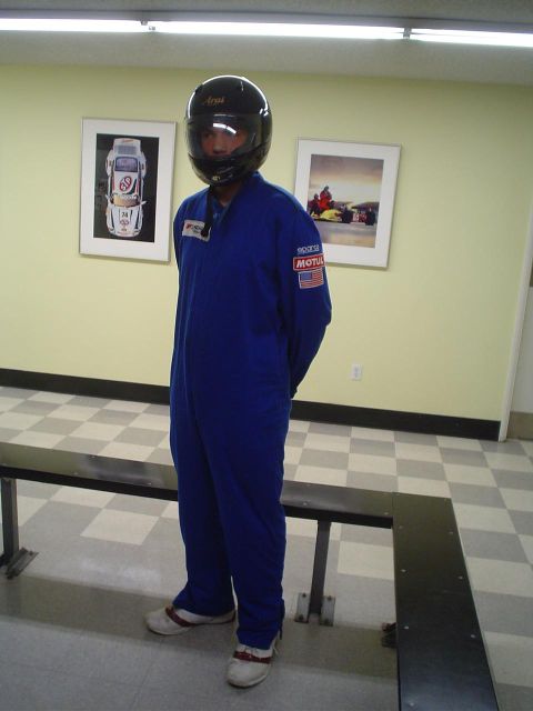 1993 Ford Taurus - A person wearing a blue racing suit and helmet stands indoors, with framed racing photographs on the wall behind them.