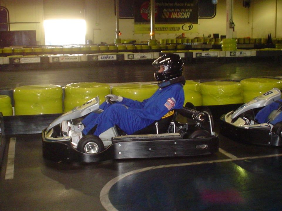 Two go-karts on an indoor track, one with a driver in a blue suit and helmet
