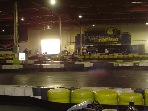 1993 Ford Taurus - Go-karts race on a track inside a building with a bright light coming from an open doorway.