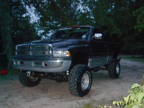 1997 Dodge 1500 - This lifted 1997 Dodge 1500 pickup truck is parked on a dirt lot with trees in the background.
