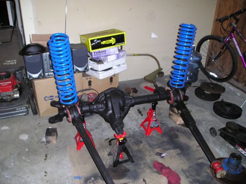 1986 Ford Bronco II - Vehicle axle assembly with blue springs, Yukon box, and lawnmower visible in garage.