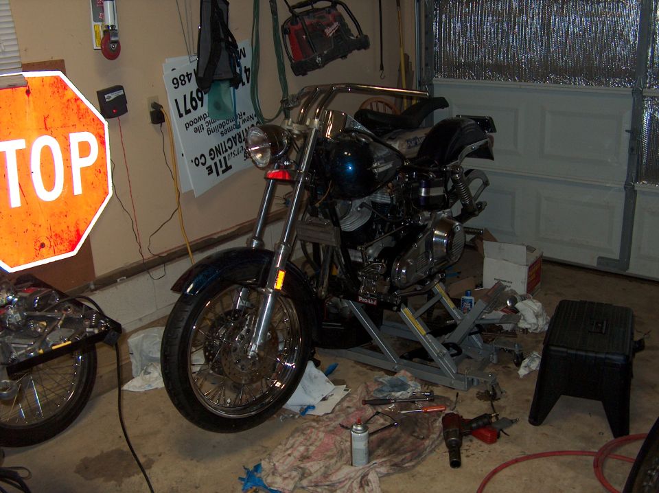 Motorcycle on a lift in a garage with tools on the floor and a stop sign on the wall
