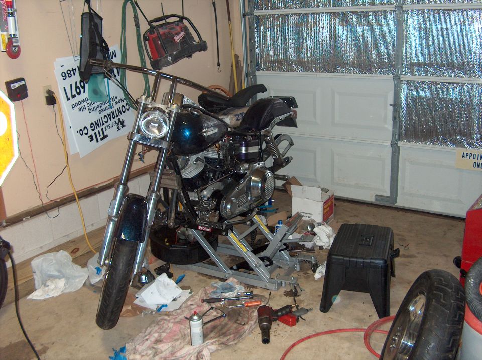 Motorcycle on a lift in a garage, with tools scattered around. It has a teal-colored fuel tank and chrome handlebars