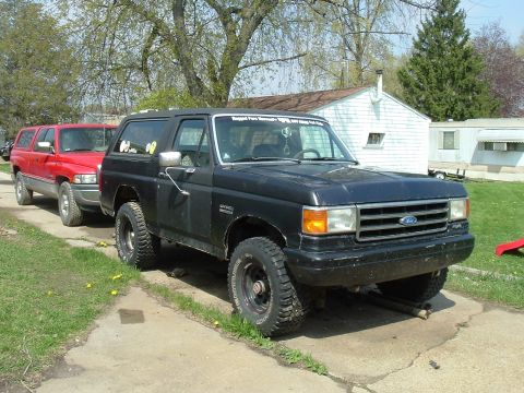 1989 Ford Bronco - A black Ford Bronco is parked on a driveway next to a red SUV.