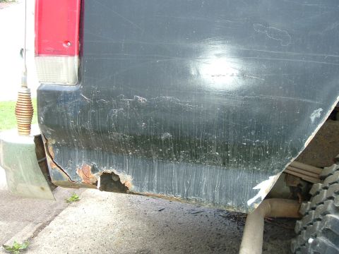 1989 Ford Bronco - The lower rear quarter panel of a vehicle shows extensive rust damage and deterioration.