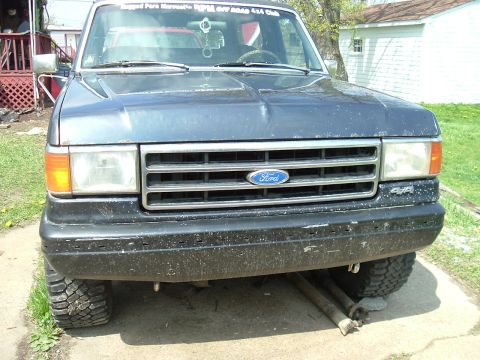 1989 Ford Bronco - Front view of a dark blue Ford Bronco with a 4x4 badge and lifted suspension, parked outdoors.