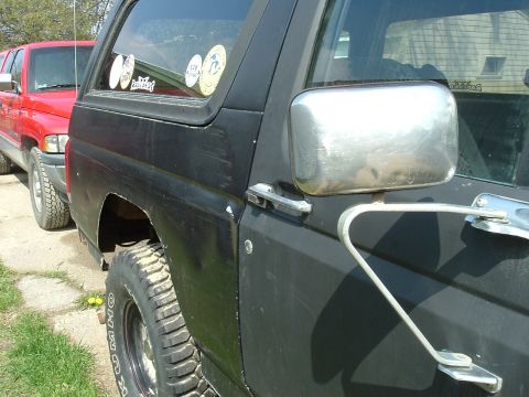 1989 Ford Bronco - Side profile of a black 1989 Ford Bronco, with a red truck visible behind it.