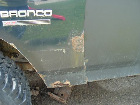 1989 Ford Bronco - Close-up of the Bronco XLT badge, showing rust damage on the vehicle's lower body.