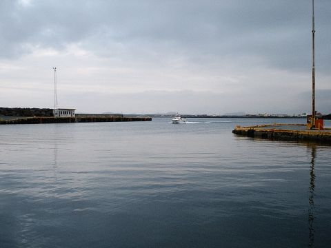 1996 Ford Bronco - A small white boat navigates the water in a harbor, with industrial structures and a distant coastline visible.